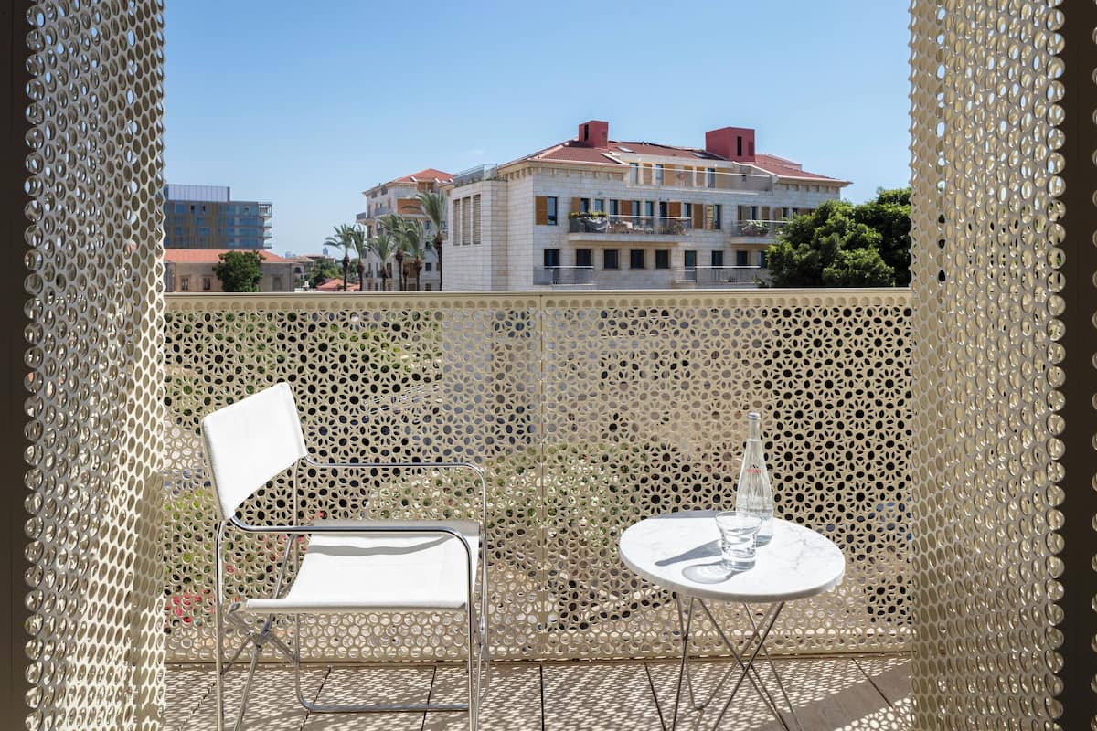 A balcony with a perforated metal screen, a white chair, and a small round table with bottles.