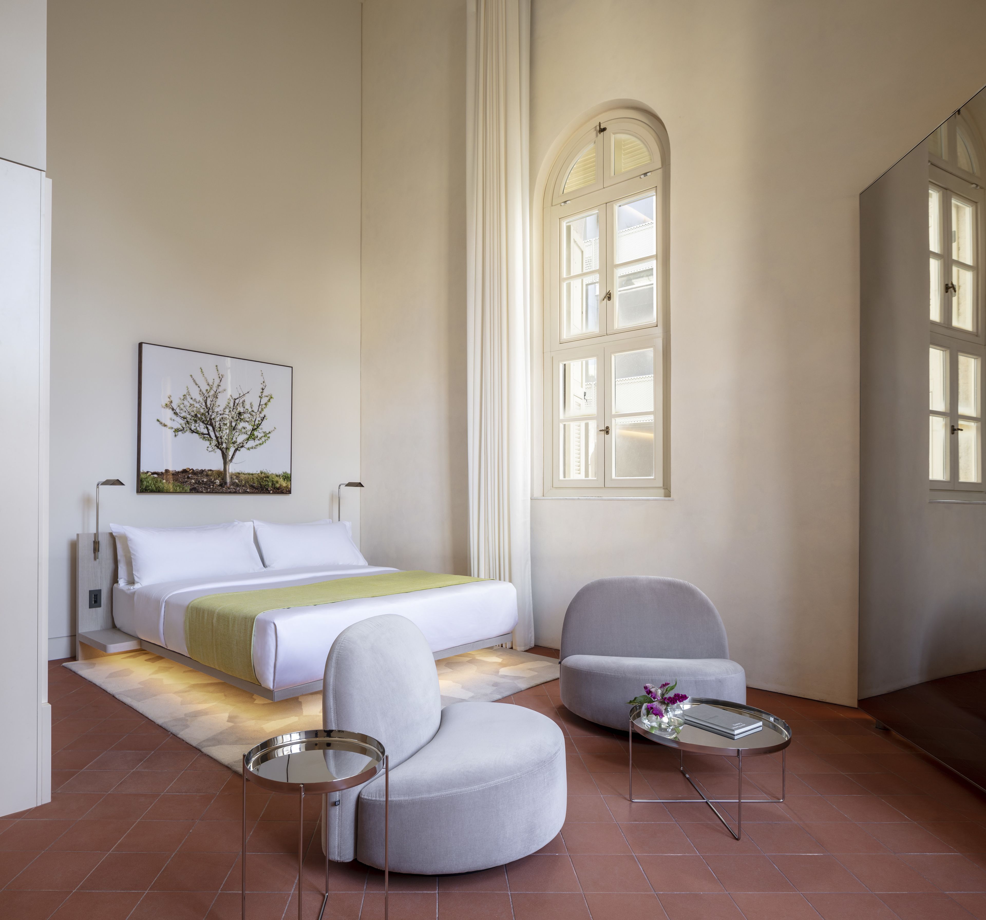 A bedroom with a bed, a chair, a small table, a picture on the wall, and a window.