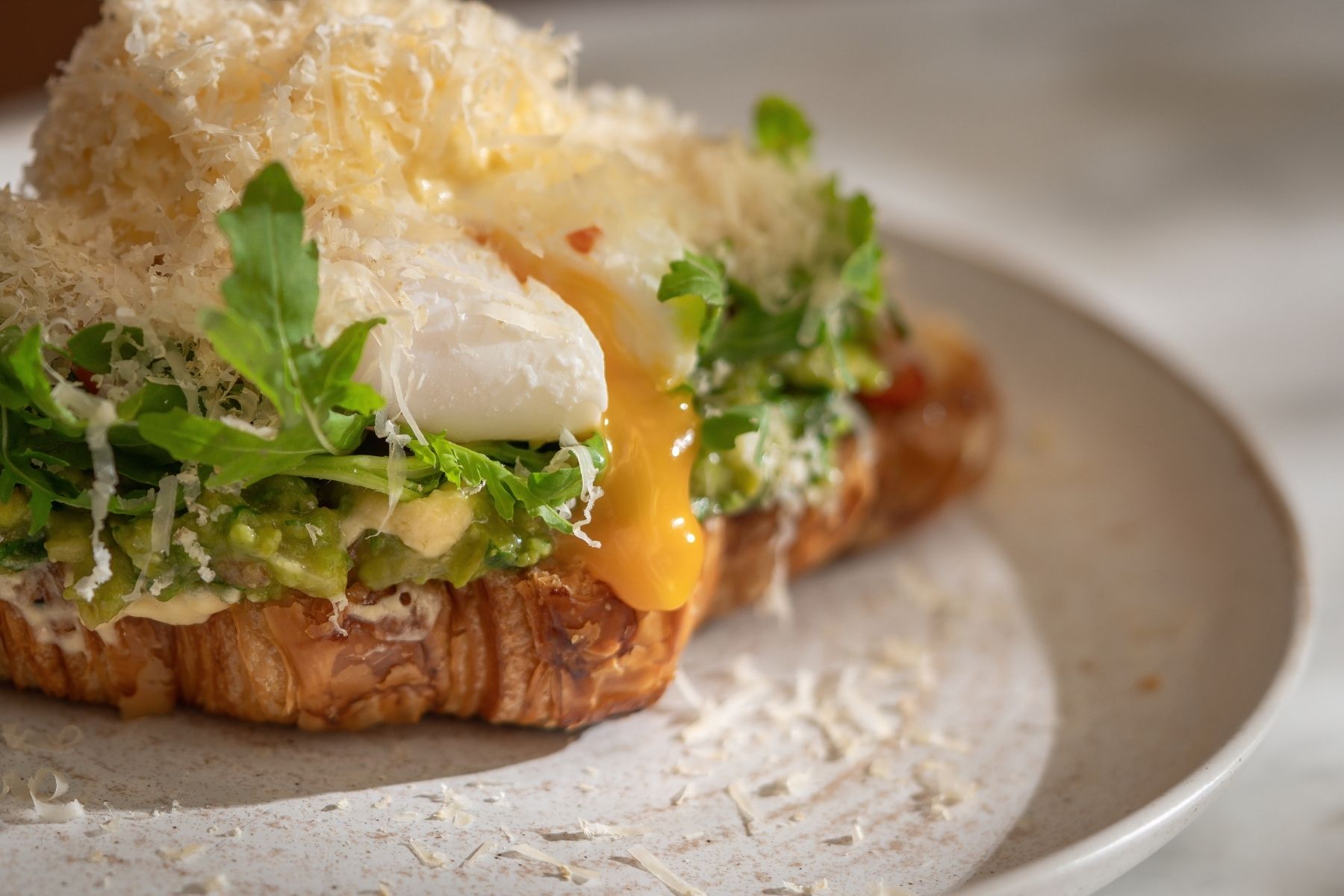 A sandwich with cheese, greens, and a poached egg on a plate.