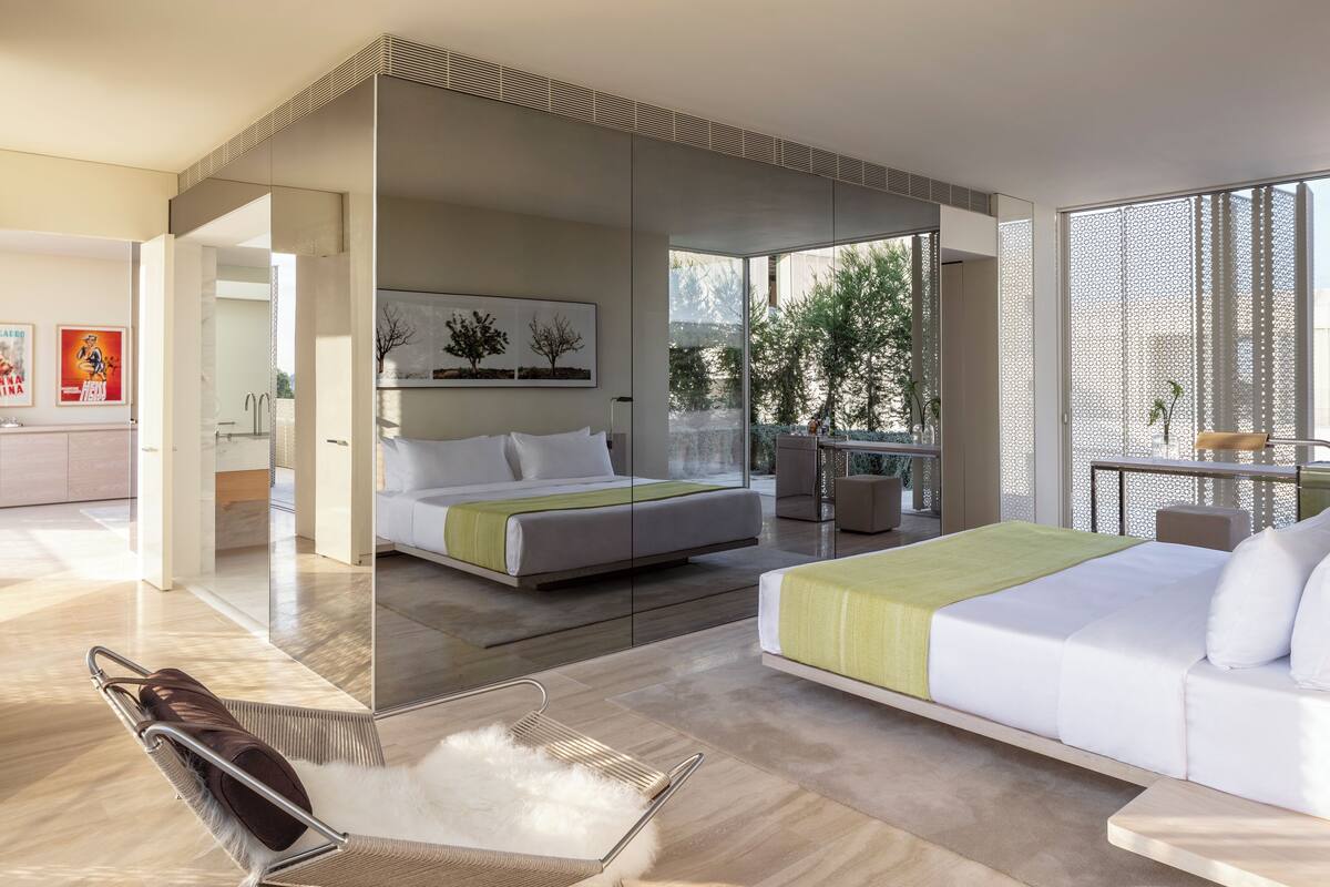 A modern hotel room with a bed, a sofa, a chair, and a balcony with a view of trees.