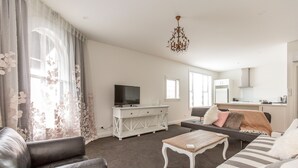 A living room with a TV, sofa, coffee table, and a dining area with a table and chairs. - Provincial Apartment 2 (Nelson)