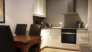 A modern kitchen with white cabinets, a black stove, and a dining area with a wooden table and chairs. - Apartm. in a family house with 2 bedr. and a living room with 2 beds (RVK)