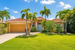 A residential house with a red-tiled roof, a garage, and a well-maintained lawn with palm trees.