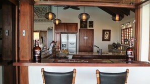 A bar area with two black chairs, wooden cabinets, a refrigerator, and hanging pendant lights. - Sea Winds Luxury Villas (Korolevu)