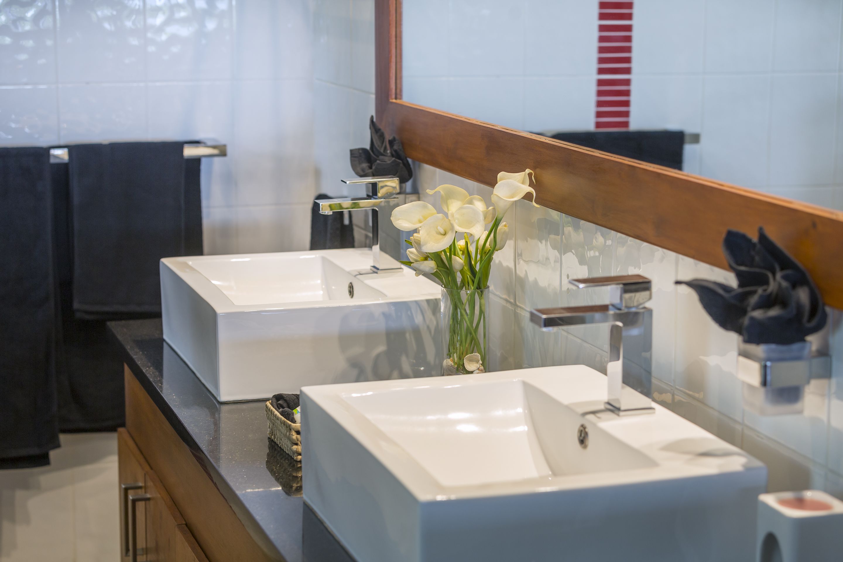 A modern bathroom with two white sinks, a large mirror, and a vase with white flowers.