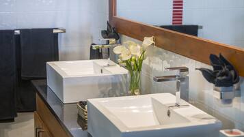 A modern bathroom with two white sinks, a large mirror, and a vase with white flowers.