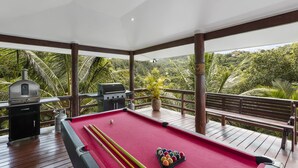 A pool table with billiard balls, a pool cue, and a grill on a wooden deck with a view of lush greenery. - Sea Winds Luxury Villas (Korolevu)