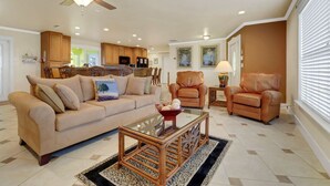 A living room with a beige sofa, a glass coffee table, a brown leather armchair, and a ceiling fan.