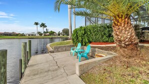 A waterfront patio with turquoise chairs, a palm tree, and a view of the water and distant buildings.