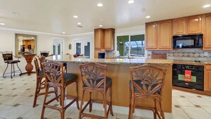 A spacious kitchen with wooden cabinets, a central island with bar stools, and a view to the outdoors.