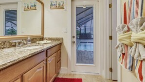 A bathroom with a granite countertop, wooden cabinets, a large mirror, and a door leading to a patio.