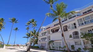 A beachfront hotel with multiple balconies, palm trees, and a clear blue sky. - Flor del Mar 1D (Punta Cana)