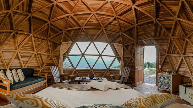 A geodesic dome room with a bed, seating area, and a view of the sea.