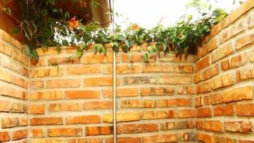 Chuveiro de canto com parede de tijolos, chuveiro pendurado e prateleira com produtos de higiene pessoal.