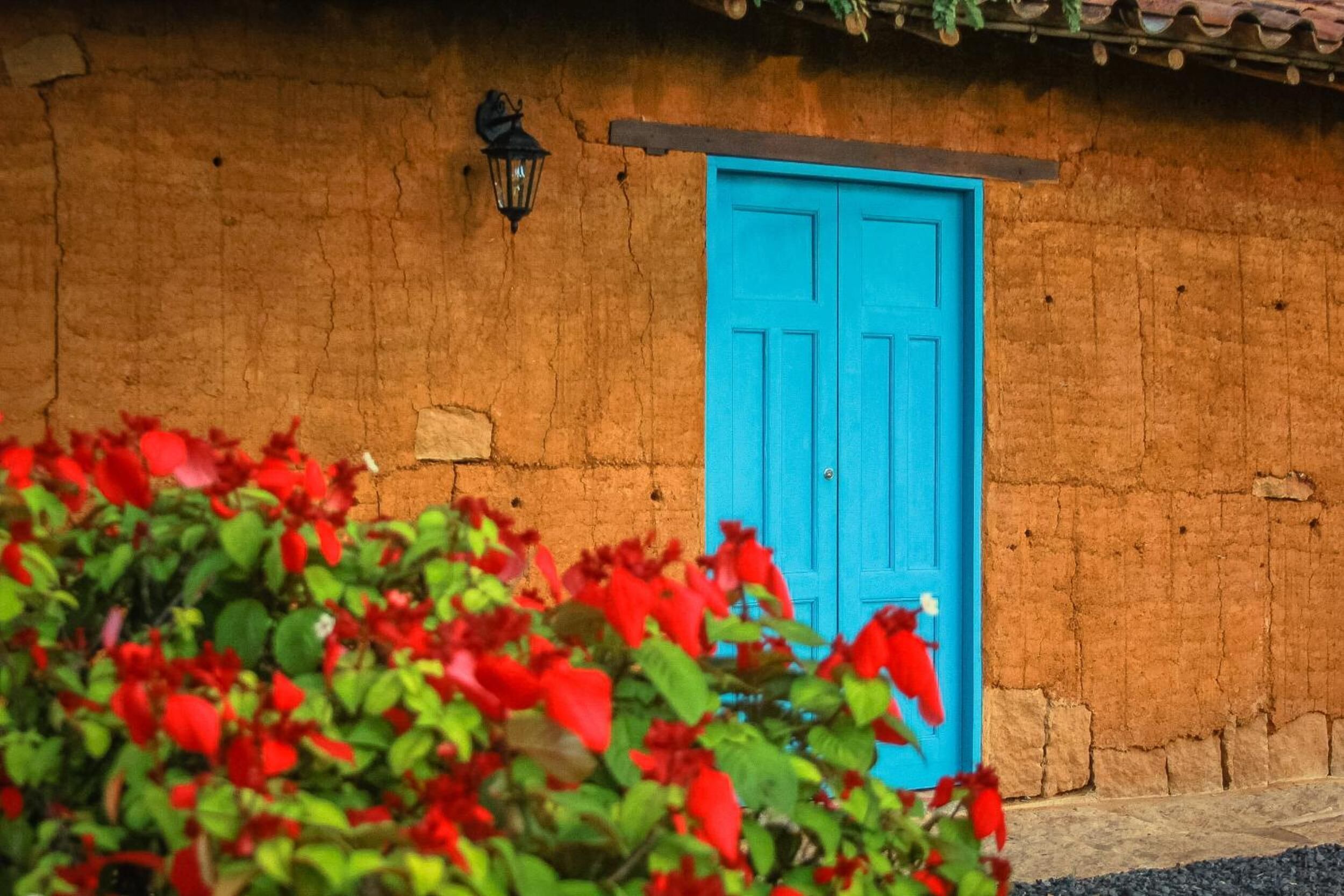 Un bâtiment rustique avec une porte bleue et une petite lanterne noire accrochée au mur.