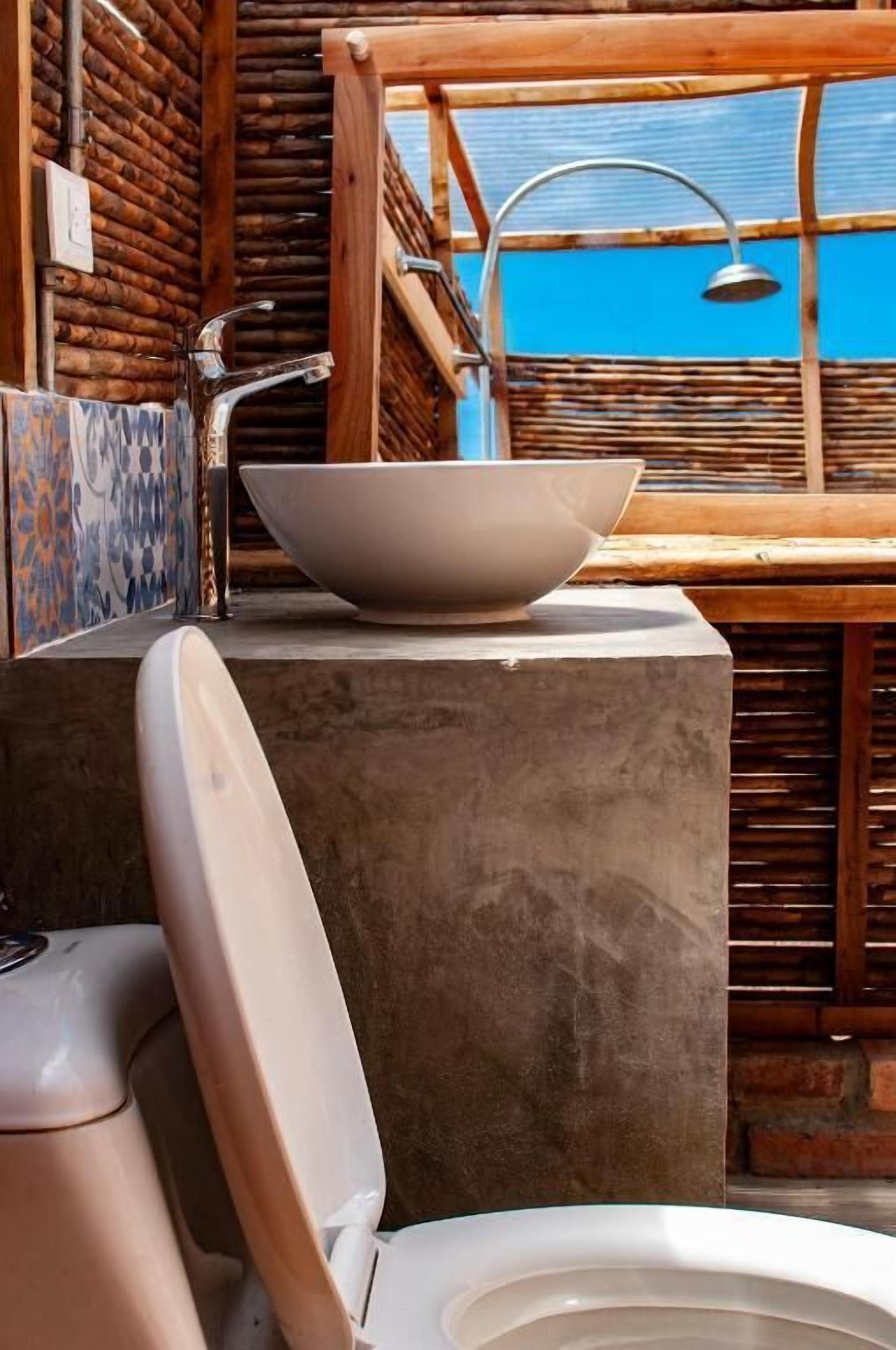 A bathroom with a modern sink, a toilet, and a shower area with a wooden structure and a blue-tiled wall.