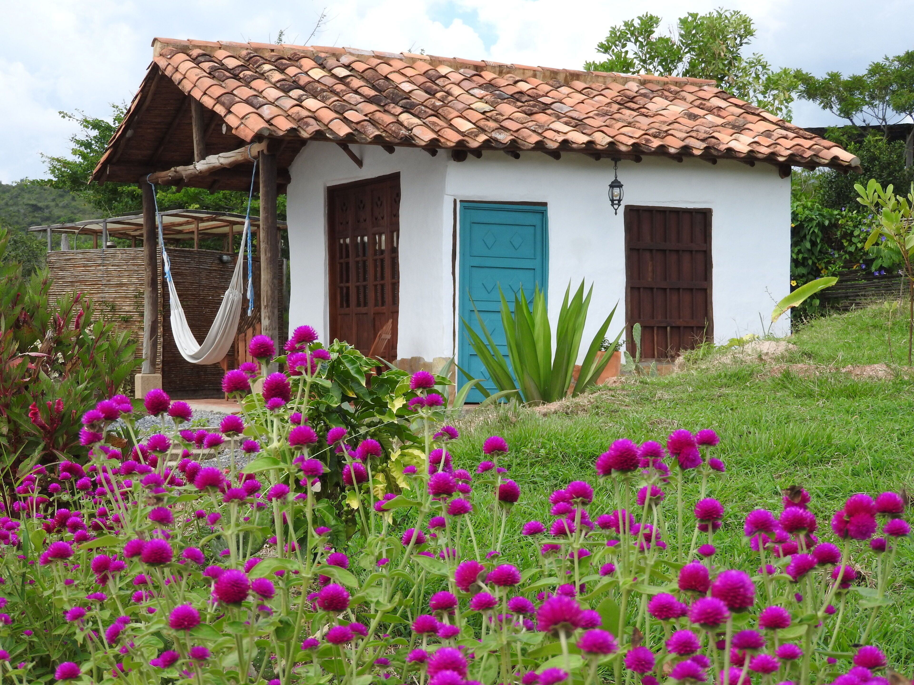Una pequeña casa blanca con techo de tejas, puerta azul y contraventanas de madera.