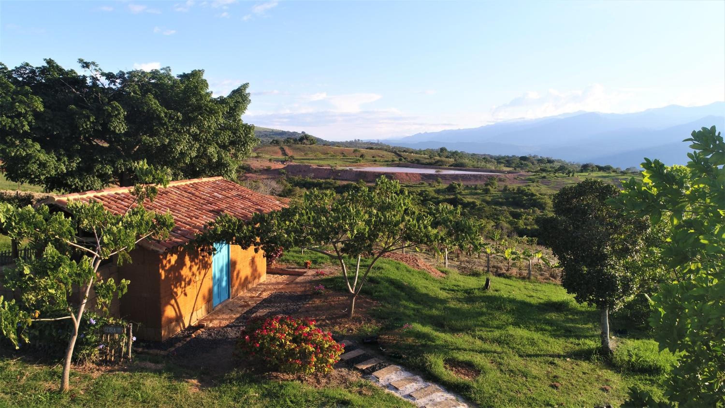 Un paysage rural avec un petit bâtiment, peut-être une ferme, entouré de verdure et avec une étendue d'eau visible au loin.