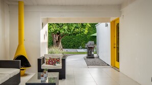 A modern outdoor lounge area with wicker furniture, a yellow chimney, and a view of a green hedge and a building in the background. - Look to the West ... on Via Miraleste! (Palm Springs)