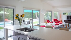 A modern kitchen with a large island, a dining area with red chairs, and a view of a swimming pool and garden. - Look to the West ... on Via Miraleste! (Palm Springs)