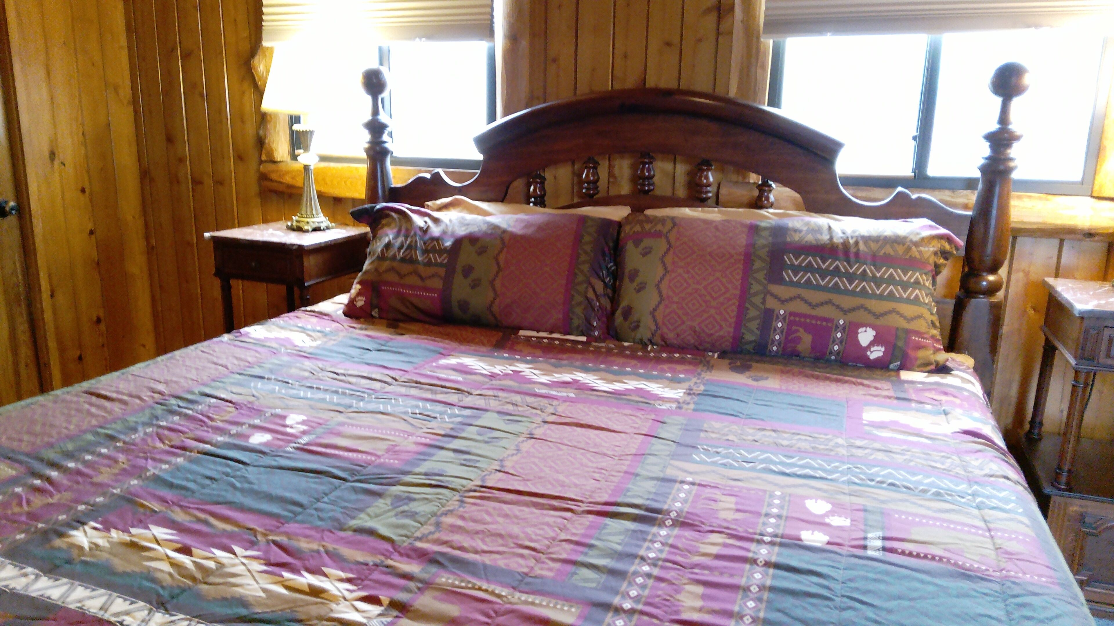Una habitación de madera con cama, mesita de noche y ventana.