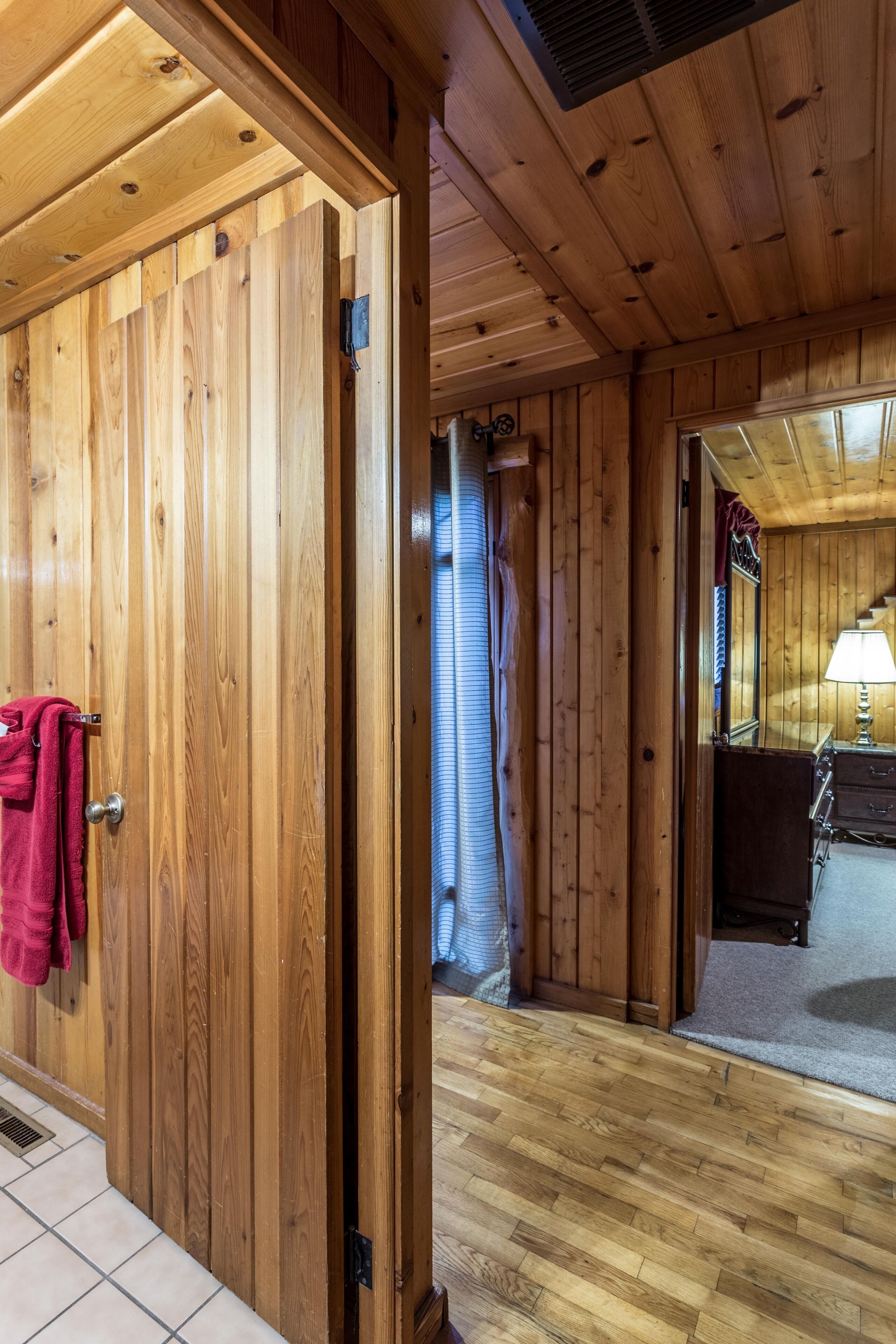 A wooden interior with a door, a towel hanging on the door handle, a lamp on a dresser, and a mirror.