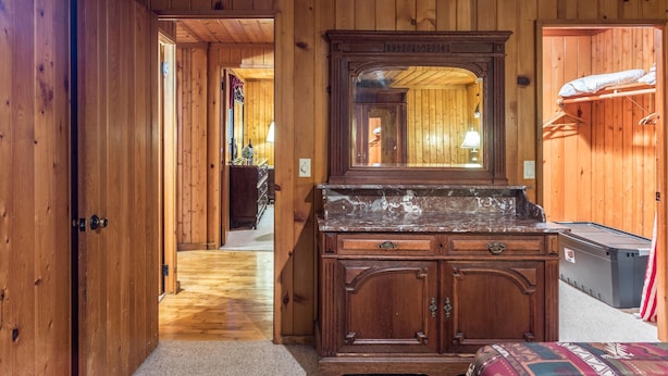 A wooden-paneled room with a large mirror above a wooden dresser, a bed with a colorful blanket, and a suitcase on the floor. - 2 BD/2BA  LOG HOME 1 1/2 MI To SDC 500 YDS TO TABLE ROCK LAKE 15 MIN TO BRANSON (Branson)