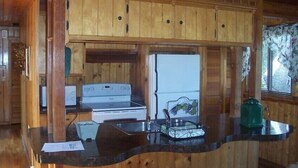 A wooden cabin interior with a kitchen area featuring a stove, refrigerator, and a counter with a sink and a green kettle. - 2 BD/2BA  LOG HOME 1 1/2 MI To SDC 500 YDS TO TABLE ROCK LAKE 15 MIN TO BRANSON (Branson)