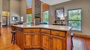 A spacious kitchen with a large island, wooden cabinets, and a stone accent wall. - Large Side Yard! 2 minutes to Table Rock Lake! (Hollister)