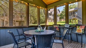 An outdoor patio with wicker furniture and a round table, featuring large windows and string lights. - Large Side Yard! 2 minutes to Table Rock Lake! (Hollister)