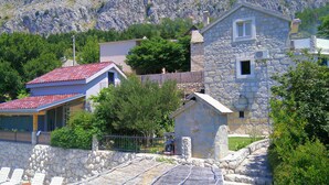 A stone building with a red-tiled roof, surrounded by greenery and a stone wall. - old stone house Lelas (Omiš)