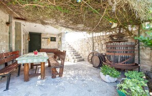 An outdoor seating area with wooden benches and a table, surrounded by stone walls and potted plants. - old stone house Lelas (Omiš)
