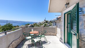 A balcony with a table and chairs, a stone wall, and a view of the sea and mountains. - old stone house Lelas (Omiš)