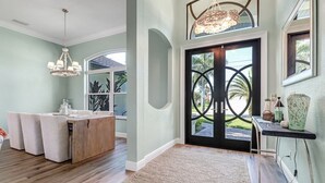 A modern kitchen with a central island, a chandelier, and a view through a glass door. - Cecilia 1015 Modern SW Cape Gulf Access Home w/ heated Pool & Spa (Cape Coral)