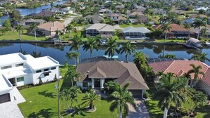 A residential area with houses, a body of water, and palm trees. - Cecilia 1015 Modern SW Cape Gulf Access Home w/ heated Pool & Spa (Cape Coral)