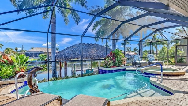A pool area with a glass enclosure, lounge chairs, and a dolphin statue. - Cecilia 1015 Modern SW Cape Gulf Access Home w/ heated Pool & Spa (Cape Coral)
