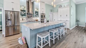 A modern kitchen with a large island, stainless steel appliances, and bar stools. - Cecilia 1015 Modern SW Cape Gulf Access Home w/ heated Pool & Spa (Cape Coral)