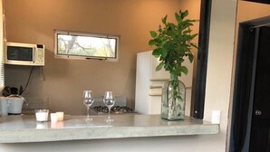 A kitchen with a bar area, two stools, a microwave, a window, and a potted plant.