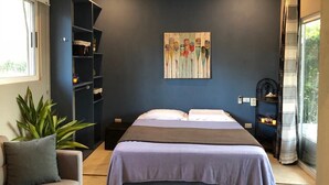A bedroom with a bed, a nightstand, a bookshelf, a painting on the wall, and a window with curtains.