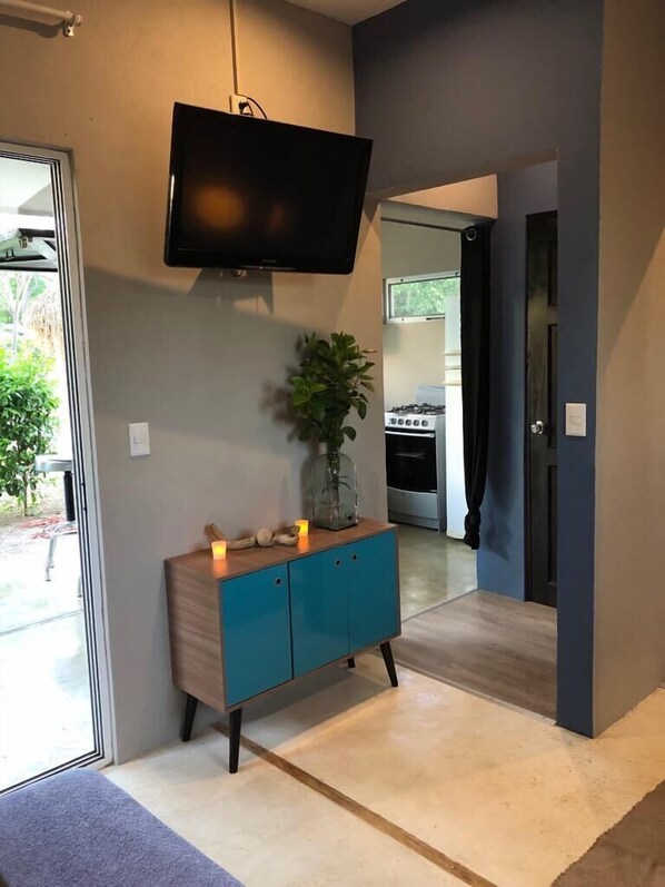 A modern interior with a teal cabinet, a flat-screen TV mounted on the wall, and a potted plant on the cabinet.