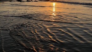A beach at sunset with waves and a clear sky.