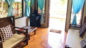 A room with a wooden sofa, a small table, and a bed. There are curtains on the windows, and a door leading outside. - KOANA Bungalows (Ko Pha-ngan)