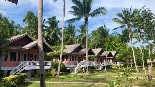 A resort with multiple bungalow-style buildings, each with a balcony and a staircase leading to the roof. The buildings are surrounded by well-maintained lawns and tall palm trees. - KOANA Bungalows (Ko Pha-ngan)