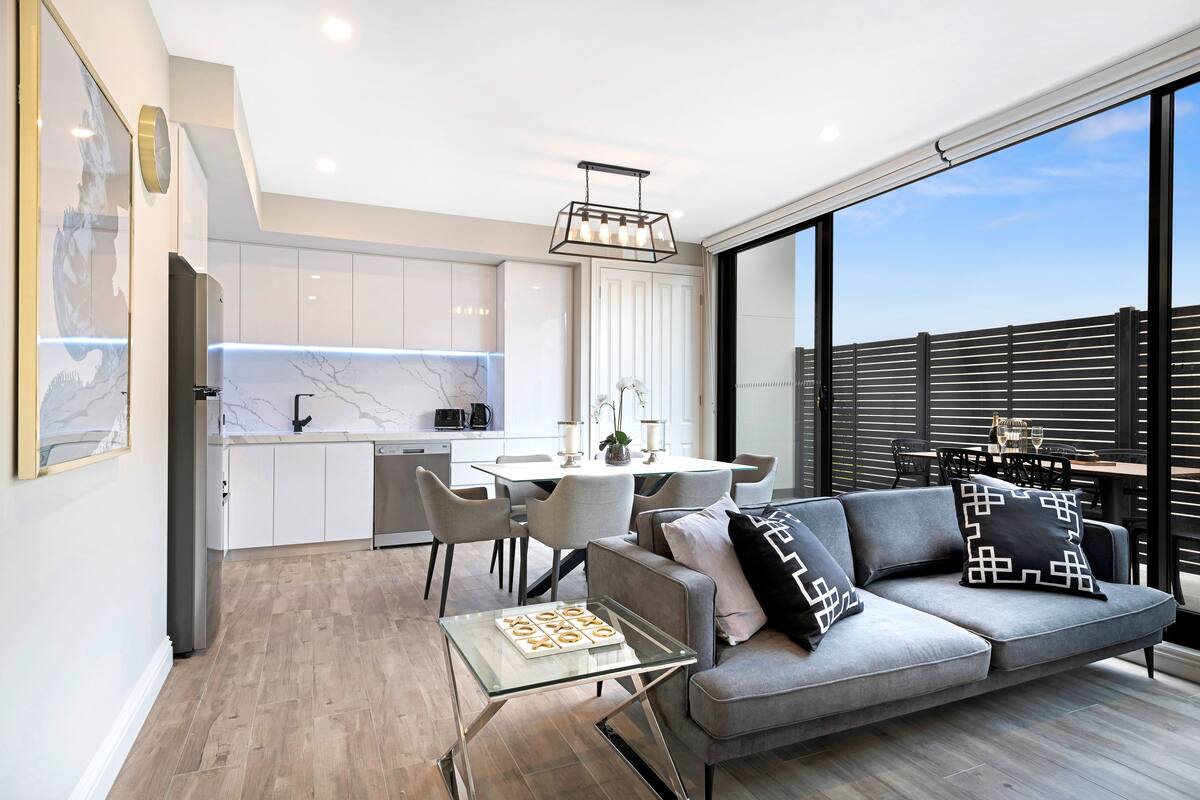 A modern living space with a grey sofa, a glass coffee table, and a dining area with a white table and chairs.