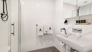 A modern bathroom with a glass-enclosed shower, white tiles, a marble countertop, and towels with a logo.