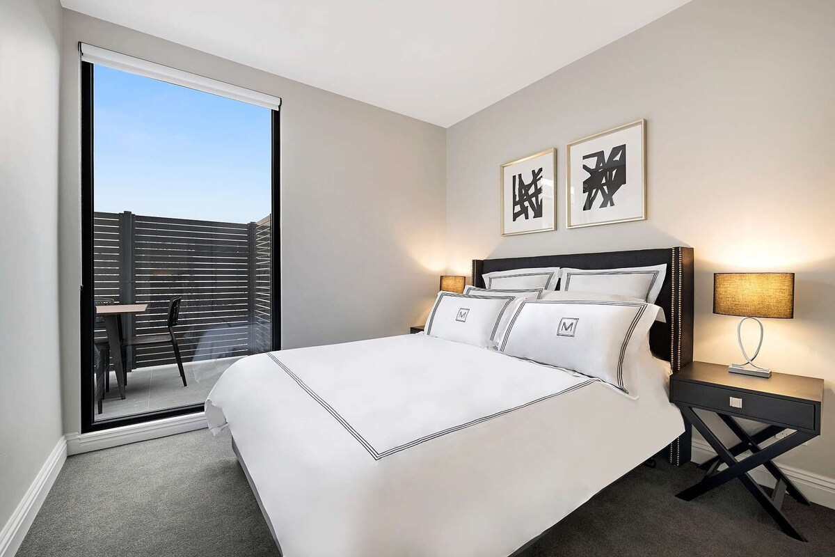 Een hotelkamer met een bed, nachtkastjes, een bureau en een balkon met uitzicht.