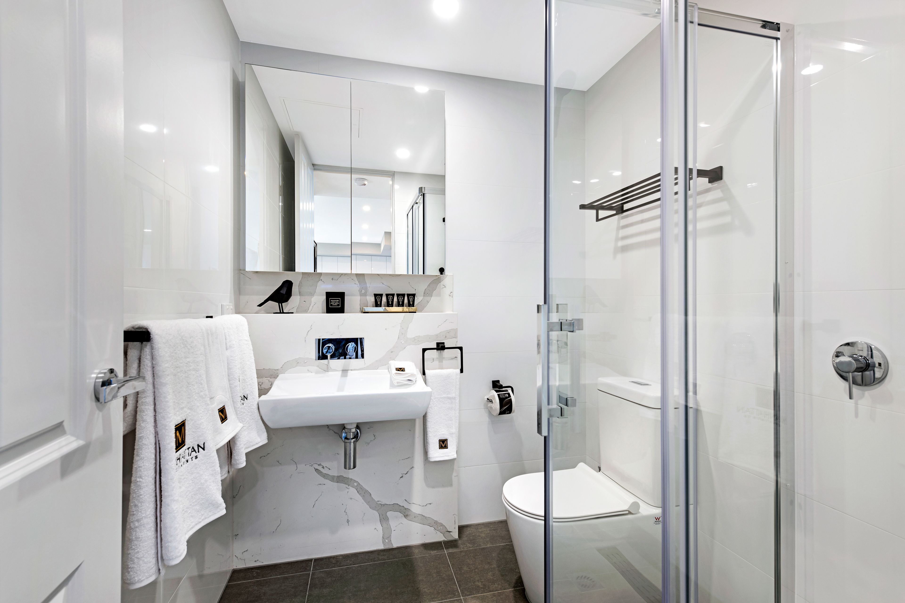 Une salle de bain moderne avec une douche à parois de verre, un lavabo blanc et un pare-baignoire en marbre.