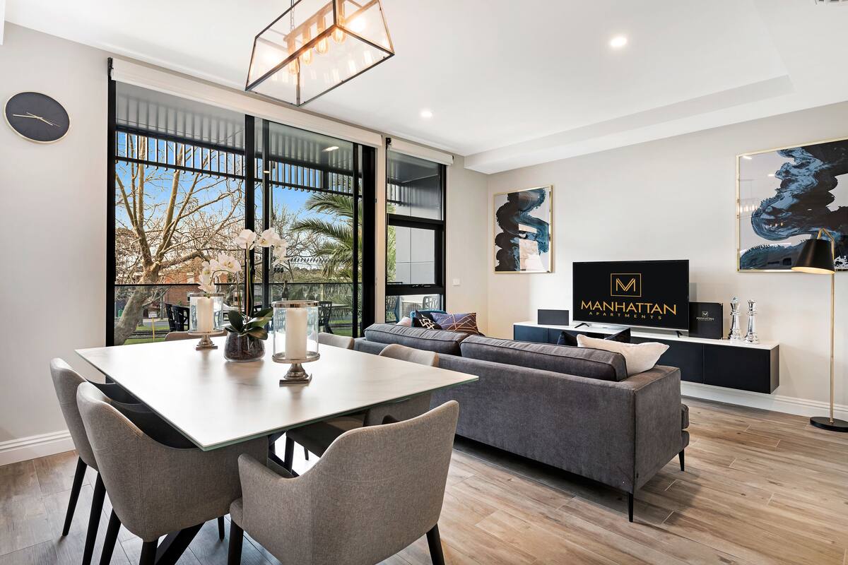 A modern living room with a dining area, large windows, and a flat-screen TV.
