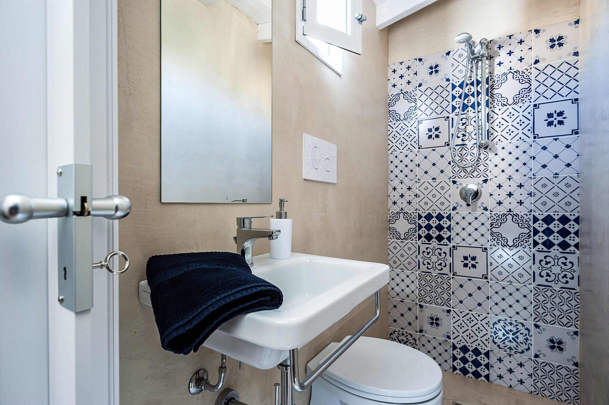 A bathroom with a white sink, a towel, a toilet, and a shower with patterned tiles.