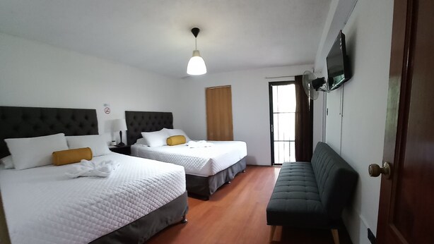 Een hotelkamer met twee bedden, een bank, een televisie en een plafondventilator.